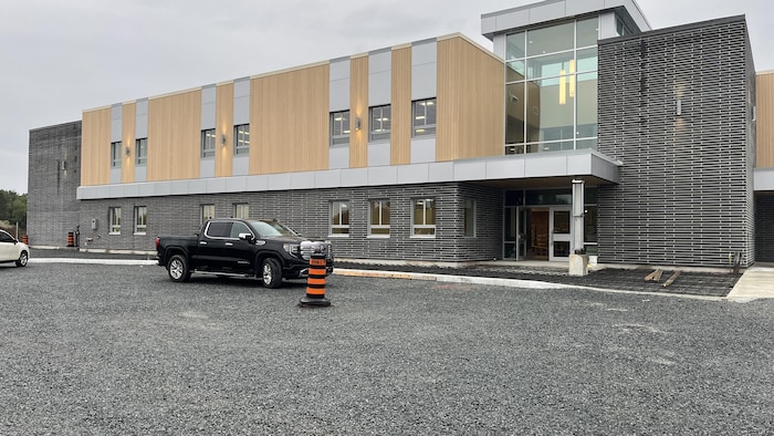Deux voitures sont stationnés dans du gravier devant une école flambant neuve de style architectural moderne.