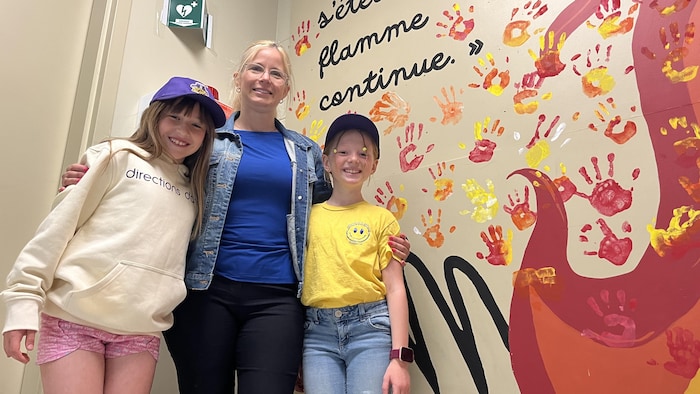 Deux élèves de l'école Notre-Dame, entoure la directrice de l'école devant une murale intérieure.