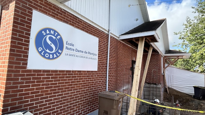 Près de la façade de l'école, il y a des matériaux de constructions et des poutres qui tiennent un petit toit.