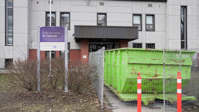 Un énorme conteneur à déchets se trouvent devant une école secondaire, en plein chantier depuis plusieurs mois. 