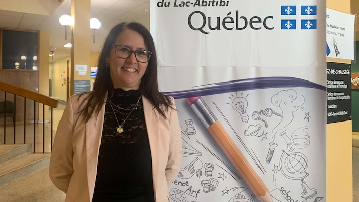 Manon Labbé prend la pose dans l'école. Elle sourit et pose à côté d'une affiche du Centre de services scolaire du Lac-Abitibi.