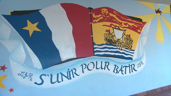 Un drapeau de l'Acadie, un drapeau du Nouveau-Brunswick et l'inscription « S'unir pour bâtir » sont peints sur un mur à l'intérieur de l'école.