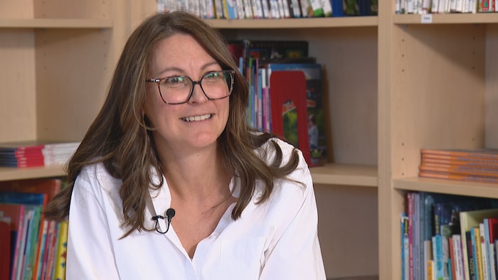 Elyse Bilodeau parle avec une bibliothèque pour enfants en arrière-plan.