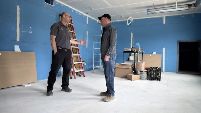 Deux hommes discutent dans une pièce en construction.