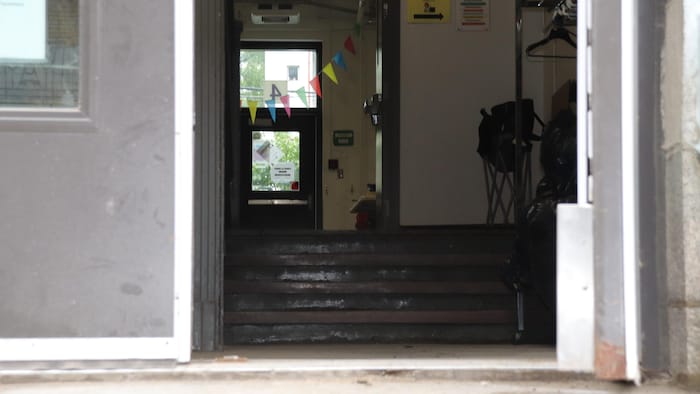 Quatre marches donnent accès à un couloir de l'école. Des fanions sont accrochés dans le corridor.