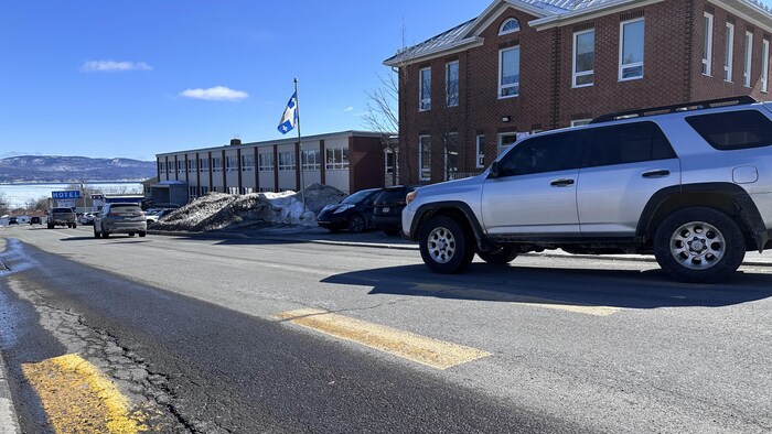 Les voitures passent devant l'école en briques rouge.