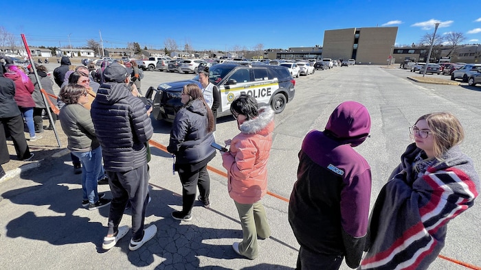 Des gens attendent devant une école. Des policiers les empêchent d'avancer.
