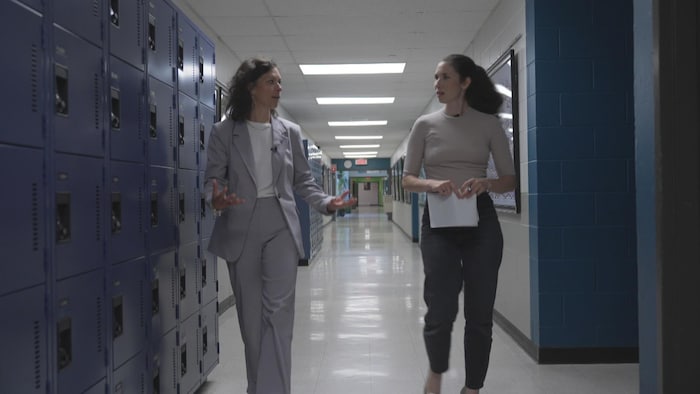 Une représentante du réseau scolaire privé discute avec une journaliste en marchant dans les corridors d'une école.