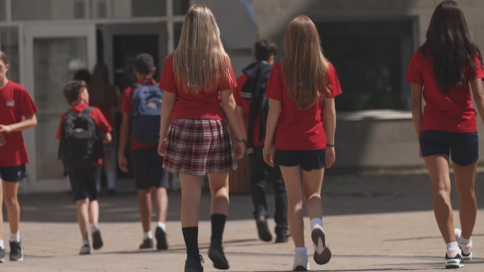 Des élèves d'une école secondaire privée marchent de dos vers la porte d'entrée de l'établissement.