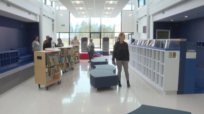 Une bibliothèque scolaire moderne et éclairée. Des étagères à roulettes sont remplies de livres.