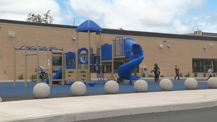 Un terrain de jeux avec des glissoires et d'autres accessoires en plastique bleu et brun, devant une école.