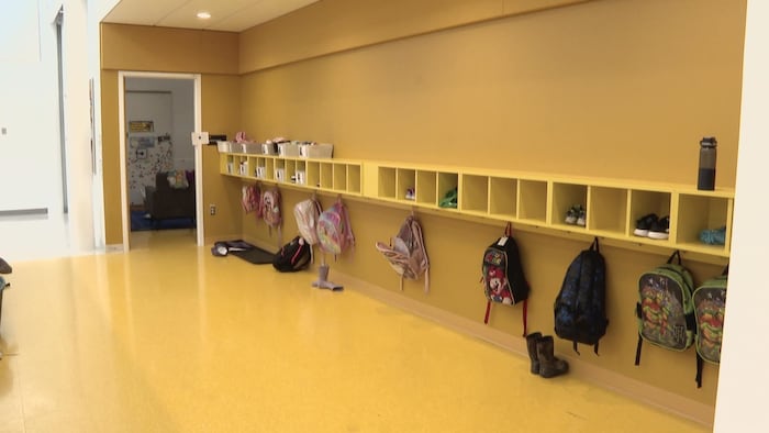Une pièce aux murs peinturés en jaune citron. Des sacs à dos d'enfants sont accrochés à des crochets.