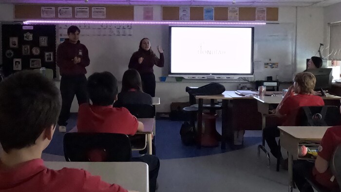 Deux jeunes font une présentation à des enfants dans une salle de classe.