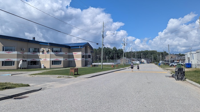 Une rue et l'école de la Première Nation de Long Point, avec deux personnes qui marchent dans la rue.