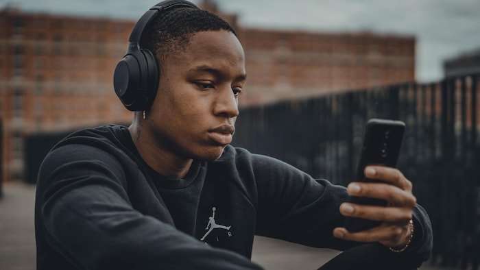 Un jeune homme, qui a un casque sur les oreilles et un téléphone dans les mains, écoute de la musique.  