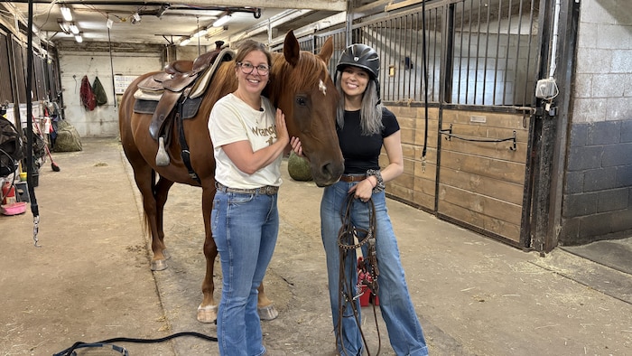 Guylaine Beaudoin et Demmi Roy-Ferguson posent dans une écurie aux côtés d'un cheval.