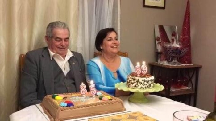A man and a woman in front of their birthday cakes.