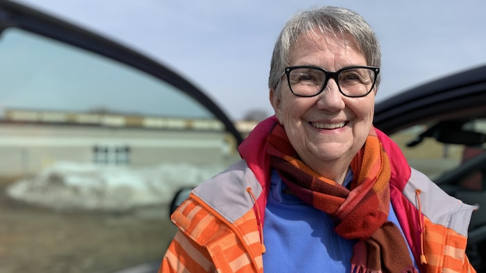 Edie Lewis, qui porte un manteau et une écharpe, sourit