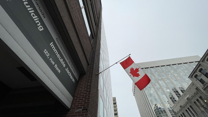 Un édifice fédéral et un drapeau du Canada qui flotte au vent.