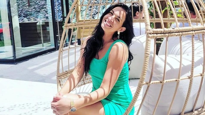 Édith Dumas est assise dans une grande chaise et elle sourit devant l'objectif.