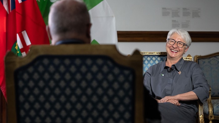 Edith Dumont est assise sur une chaise dans son bureau à Queen's Park, en face d'un journaliste et sourit.