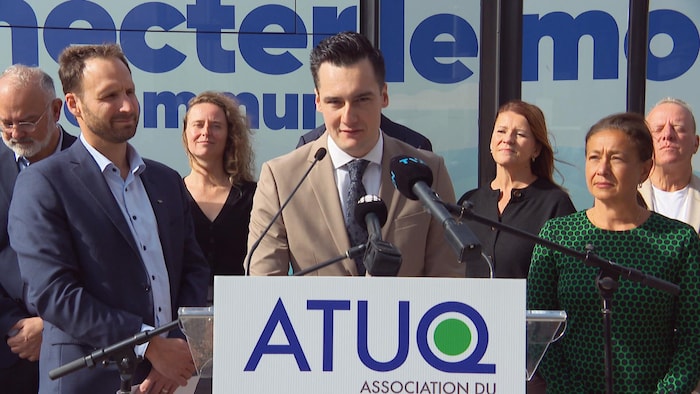 Les membres de l’ATUQ lors d’une conférence de presse présentée à l’extérieur, en été, devant un autobus.