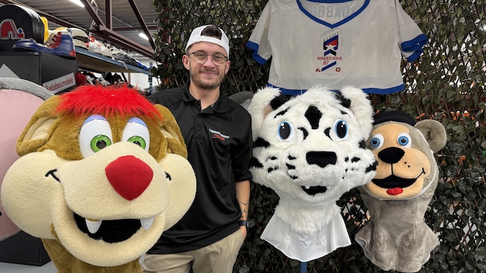Un homme sourit pour la photo aux côtés de tête de mascottes.