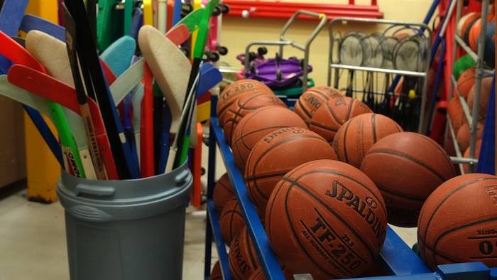 Des ballons de basketball et des bâtons de hockey dans l'entrepôt d'un gymnase d'une école primaire.