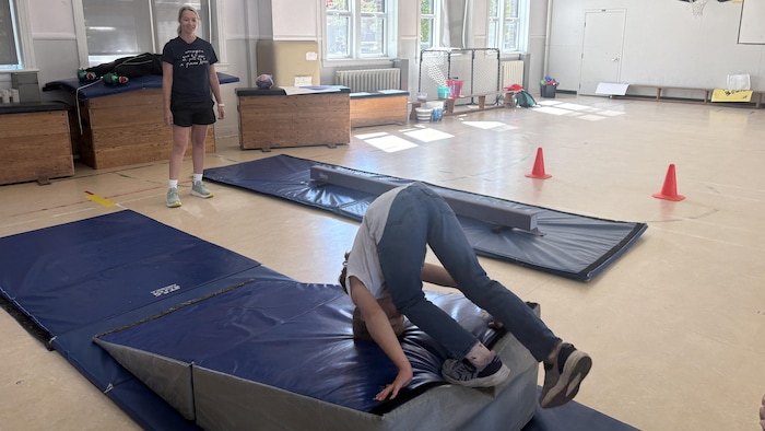 Un enfant fait une culbute dans un gymnase.