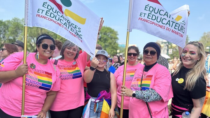 Un jour d'été, un groupe de cinq femmes et une jeune fille souriantes tiennent des drapeaux d'Éducatrices et éducateurs francophones du Manitoba. Sur leurs chandails on peut lire les mots «Gentillesse, paix, équité, amour, inclusion, diversité».