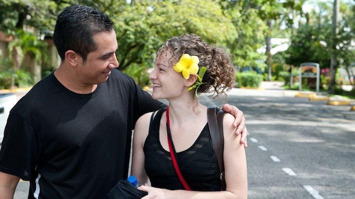 Espinal con su brazo alrededor de los hombros de su esposa, Karen Spring, de pie en una carretera bordeada de árboles en Honduras.