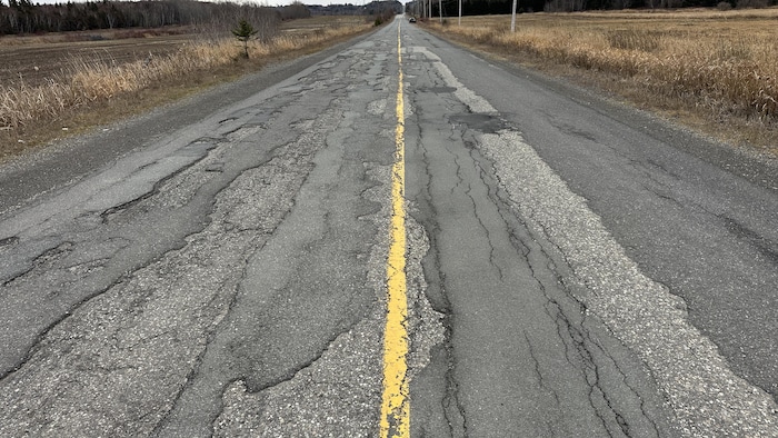 Une route rurale avec plusieurs trous, fissures et portions anciennement réparées.