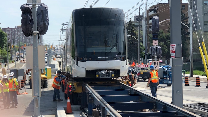 Des travailleurs installent un train léger sur les rails de la ligne Eglinton Crosstown en juin 2021.