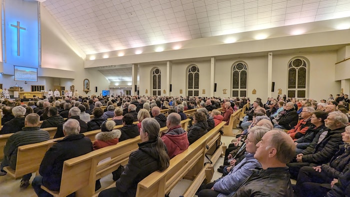 Des centaines de personnes sont assises sur les bancs d'une église pour assister à une messe.