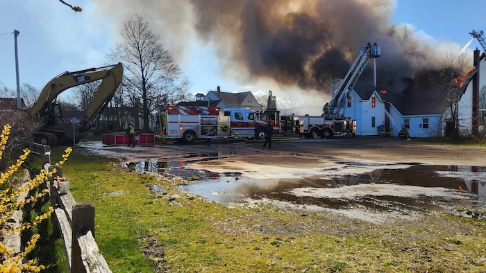 Des pompiers tentent d'éteindre le feu qui ravage une église blanche en bois.