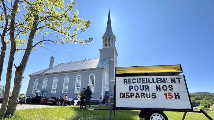 Une affiche qui indique le lieu de la cérémonie de recueillement devant une église aux Bergeronnes.