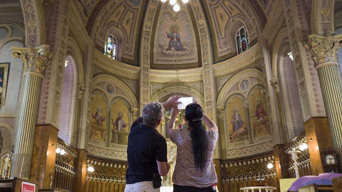 Un homme et une femme regarde le plafond d'une église. La femme est en train de tenir une tablette électronique dans ses mains.