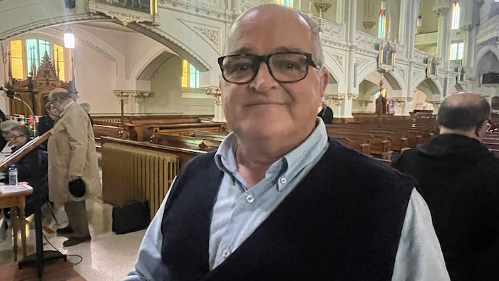 Lucien Dubé est dans une église, il sourit à la caméra.