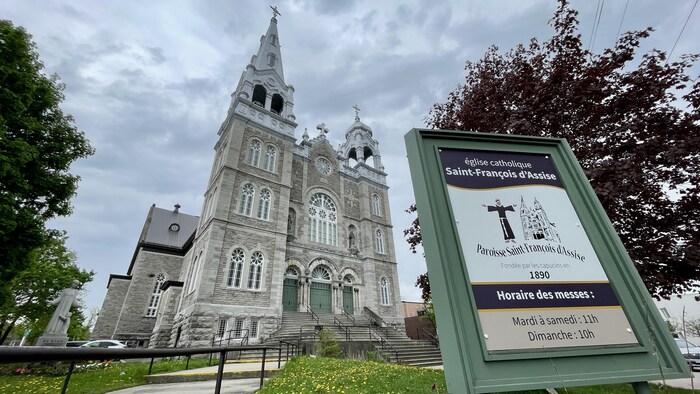 L'église Saint-François d'Assise avec, en avant-plan, un panneau d'horaires des messes.