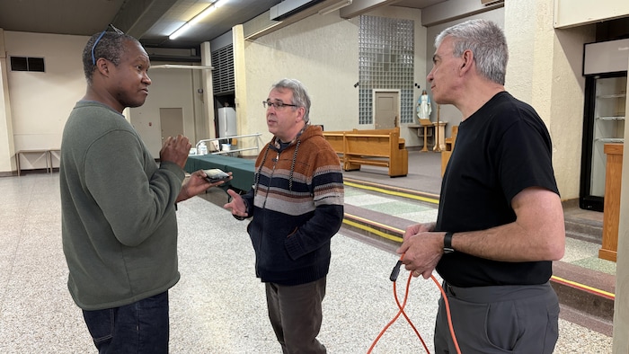 Trois hommes discutent au sous-sol de l'église Saint-Fidèle.