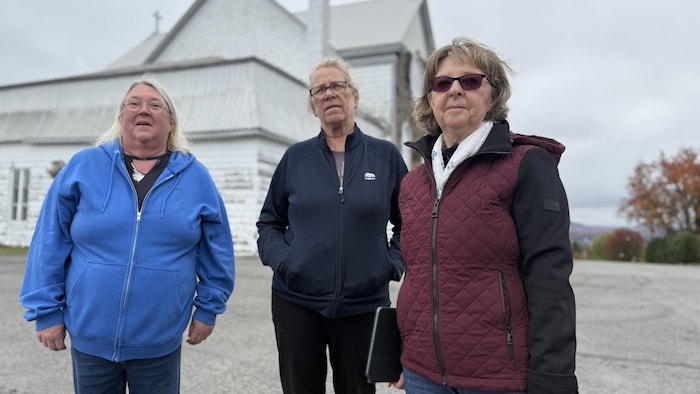 Trois femmes debout sur le terrain asphalté à l'arrière de l'église.