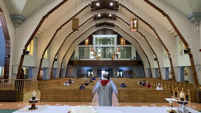 Un curé donne une messe dans une église où les fidèles sont assis à une bonne distance l'un de l'autre.