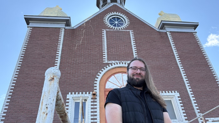 Alexander Walosik prend la pose devant l'église ukrainienne de Val-d'Or en souriant légèrement à la caméra.