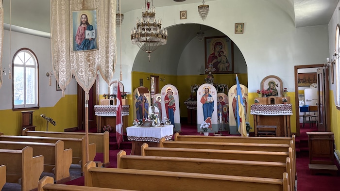 Des portraits de saints personnages et des rangées de bancs à l'intérieur de l'église ukrainienne de Val-d'Or.