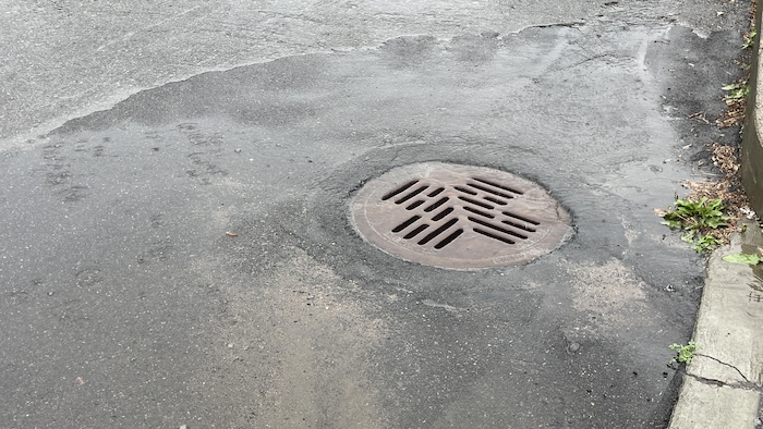 Une bouche d'égout pluvial sur une chaussée en asphalte sous la pluie.