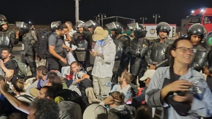 Des gens sont assis à terre et des officiers sont autour d'eux.