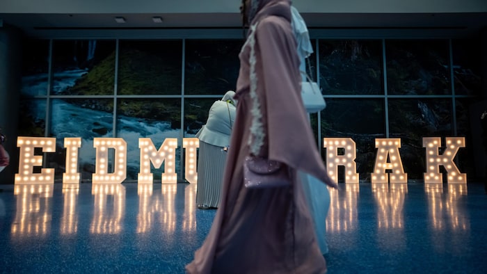 Une personne marche devant une enseigne illuminée qui dit EID MUBARAK.