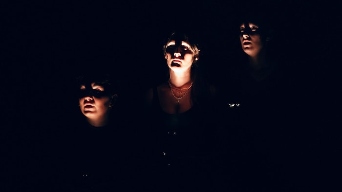 Trois visages de femmes illuminés dans le noir.