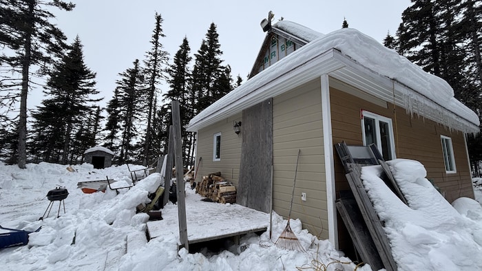 Maison dans le bois entourée de neige. Un grand panneau de bois cache une entrée ou une fenêtre.