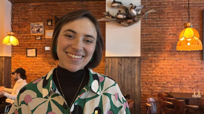 Elainie Lepage sourit à la caméra devant un mur de briques.